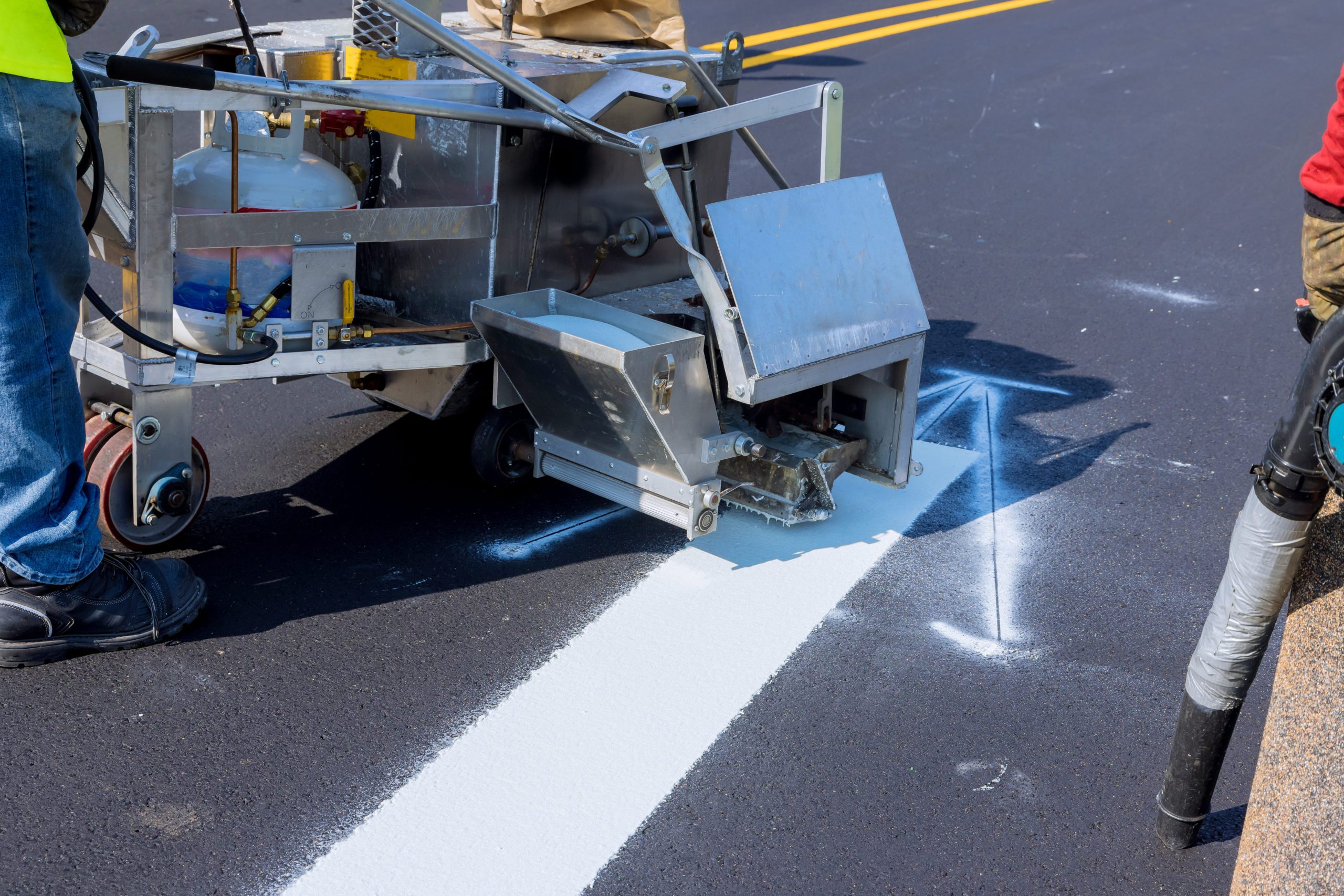 Workers apply white paint a road marking the stripes with a reflective powder on the new asphalt